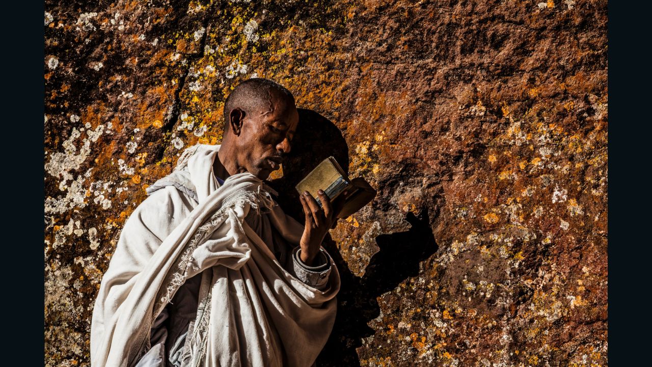 A pilgrim reading a bible and pressing his cheek to the holy walls of a church at Lalibela.