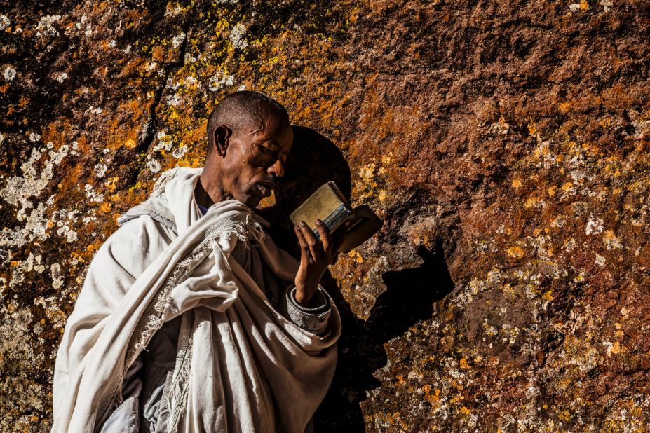 A pilgrim reading a bible and pressing his cheek to the holy walls of a church at Lalibela. Up to 100,000 pilgrims travel to this devotional site every year, many of them on foot and without shoes.