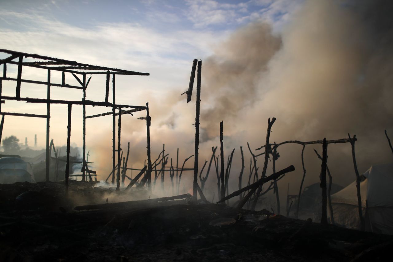 The remains of makeshift structures smolder from fires that broke out overnight in parts of the camp on October 26.