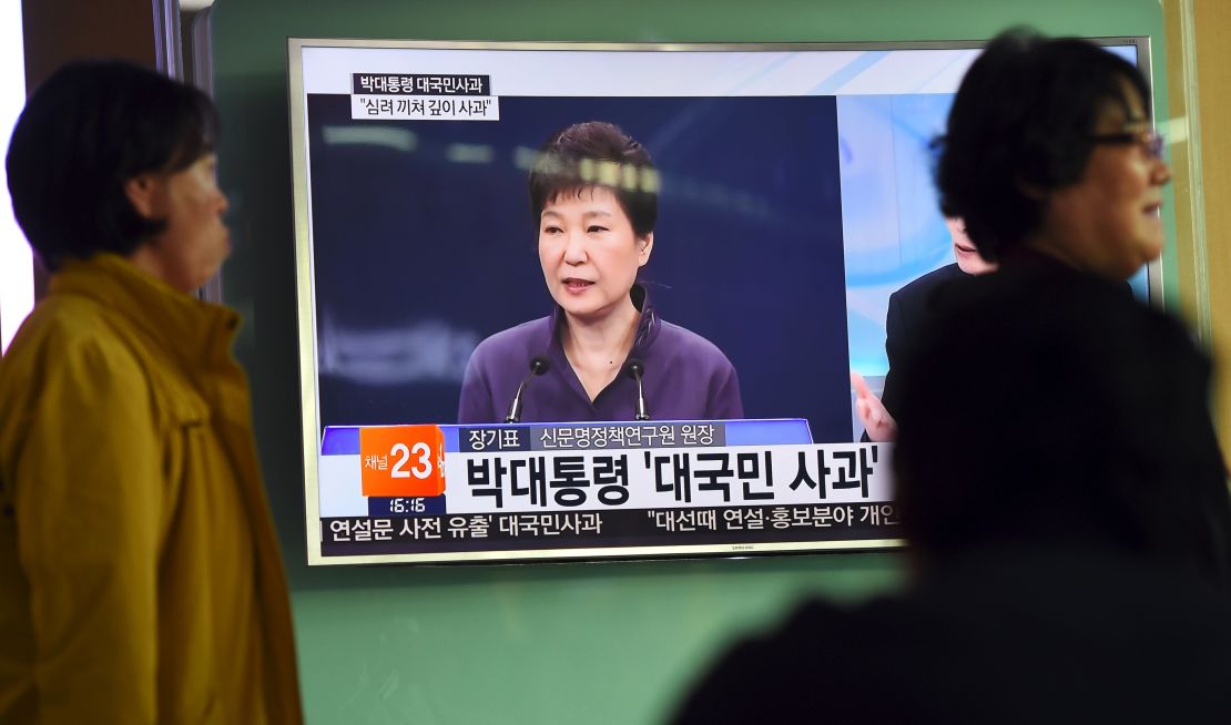 People walk past a television screen showing South Korean President Park Geun-Hye making a public apology on October 25.