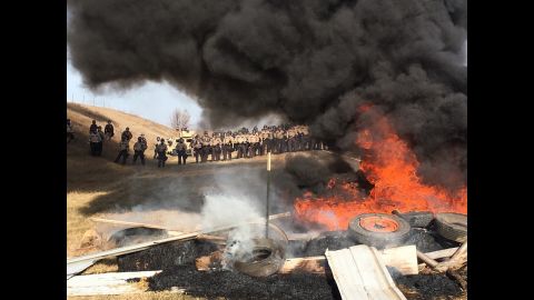Tires burn as armed soldiers and law enforcement officers stand in formation to force Dakota Access Pipeline protesters off the private land in Morton County.