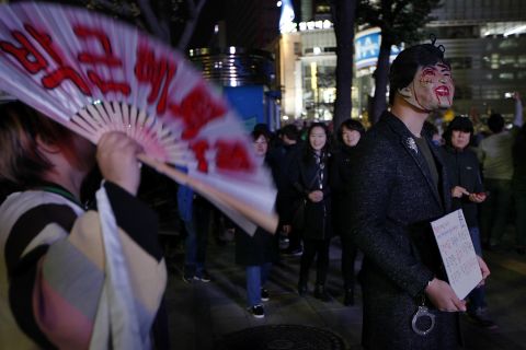 A protester wearing a mask of Park Geun-Hye holds a placard saying "Why do you need Halloween fest? We can see all the horror in our lives," during the protest.
