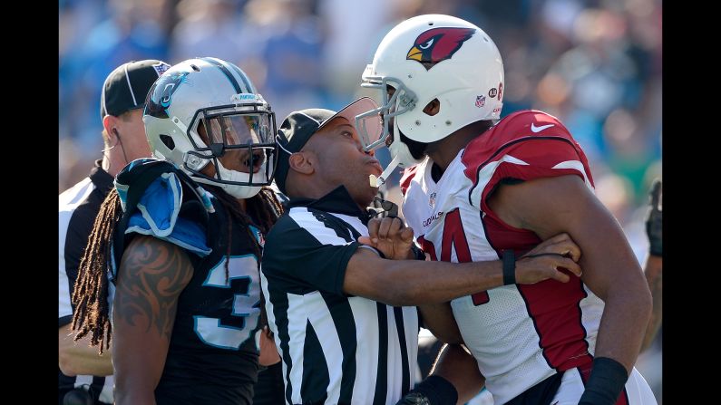 An official stands between Carolina's Tre Boston, left, and Arizona's Jermaine Gresham during an NFL game in Charlotte, North Carolina, on Sunday, October 30.