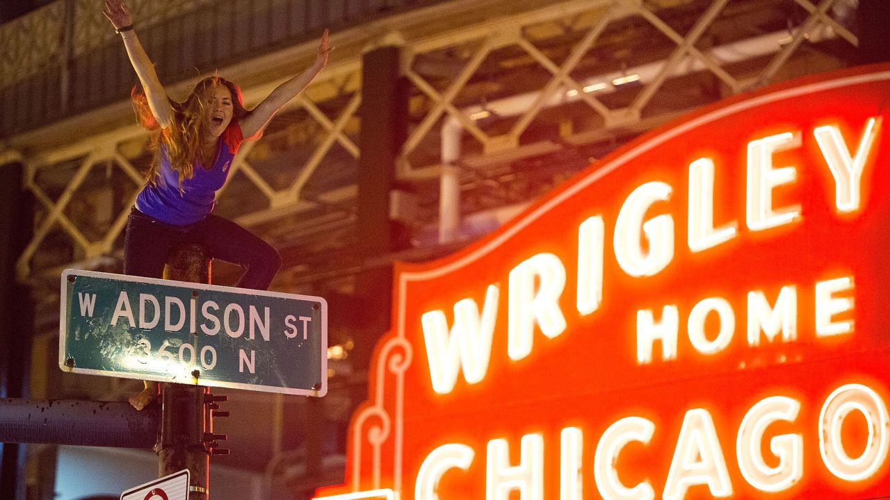 A Chicago fan straddles a street pole outside Wrigley Field as people gather to celebrate the Cubs' dramatic win. 