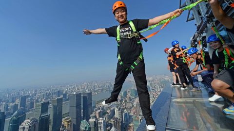 This photo taken on July 25, 2016 shows a visitor (L) balancing on an open-air glass walkway with other visitors outside the 88th floor of Jinmao Tower in the Lujiazui area of Shanghai. The 60-metre long and 1.2-meter wide walkway is officially open to the public from July 28. / AFP / STR / China OUT (Photo credit should read STR/AFP/Getty Images)