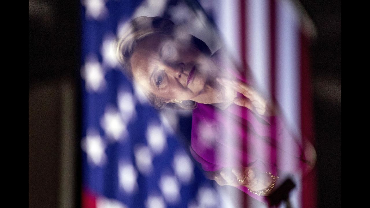 Clinton, seen in a reflection, applauds as her former primary rival, U.S. Sen. Bernie Sanders, campaigns for her in Raleigh, North Carolina, on Thursday, November 3.