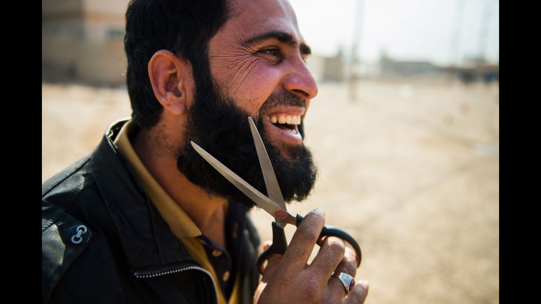 An Iraqi man who fled the fighting in Mosul uses a pair of scissors to trim his beard.