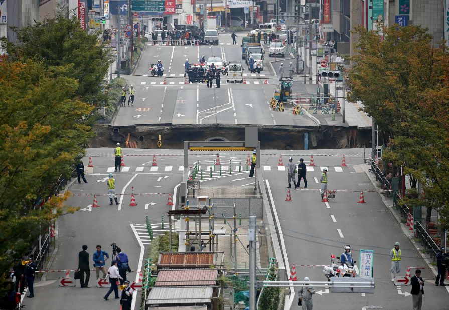 This photo shows a giant sinkhole (C) in a five-lane urban boulevard, eroding soil and exposing underground steel columns supporting commercial buildings in Fukuoka, southwestern Japan, on November 8, 2016. No injuries were reported as the accident occurred in the early morning hours. / AFP / JIJI PRESS / STR / Japan OUT (Photo credit should read STR/AFP/Getty Images)
