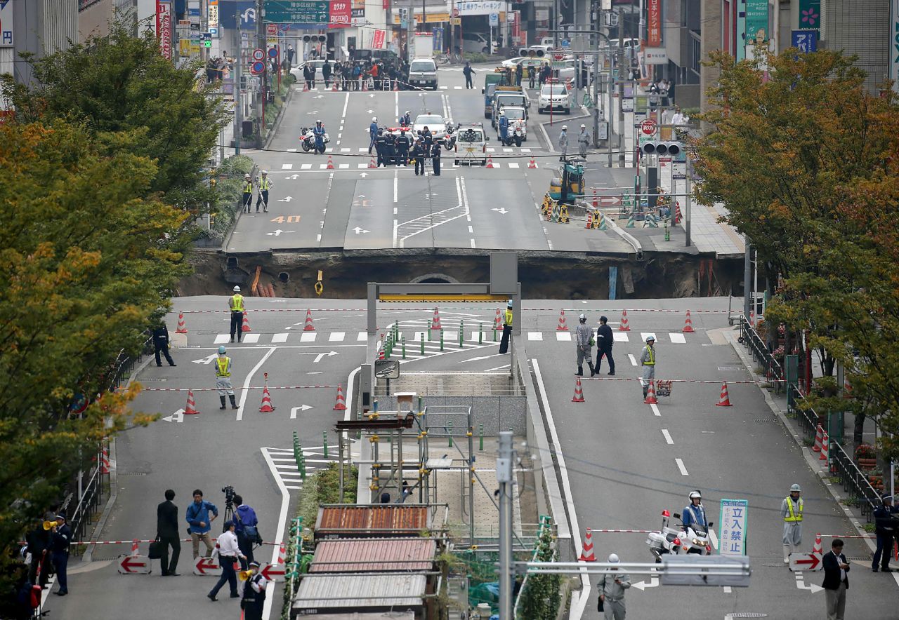This photo shows a giant sinkhole (C) in a five-lane urban boulevard, eroding soil and exposing underground steel columns supporting commercial buildings in Fukuoka, southwestern Japan, on November 8, 2016. No injuries were reported as the accident occurred in the early morning hours.      / AFP / JIJI PRESS / STR / Japan OUT        (Photo credit should read STR/AFP/Getty Images)