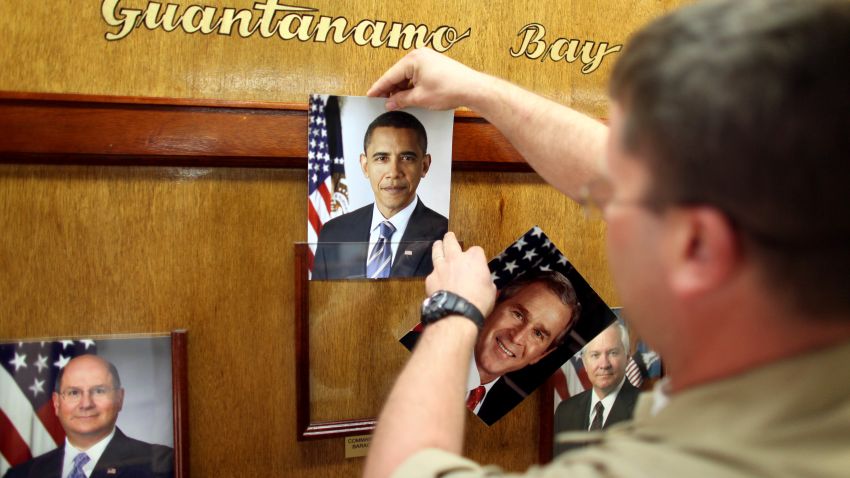 GUANTANAMO BAY, CUBA - JANUARY 20:  (NOTE TO EDITORS: PHOTO HAS BEEN REVIEWED BY US MILITARY OFFICIALS) U.S. Navy Chief Petty Officer Bill Mesta replaces an official picture of outgoing President George W. Bush with that of newly- sworn-in U.S. President Barack Obama, in the lobby of the headquarters of the U.S. Naval Base January 20, 2009 in Guantanamo Bay, Cuba.  Bush's eight-year presidency, which has overseen the detention of prisoners at Guantanamo and elsewhere, concluded midday today, and President Barack Obama has said he intends to close the offshore prison and move the trials to U.S. courts. (Photo by Brennan Linsley-Pool/Getty Images)