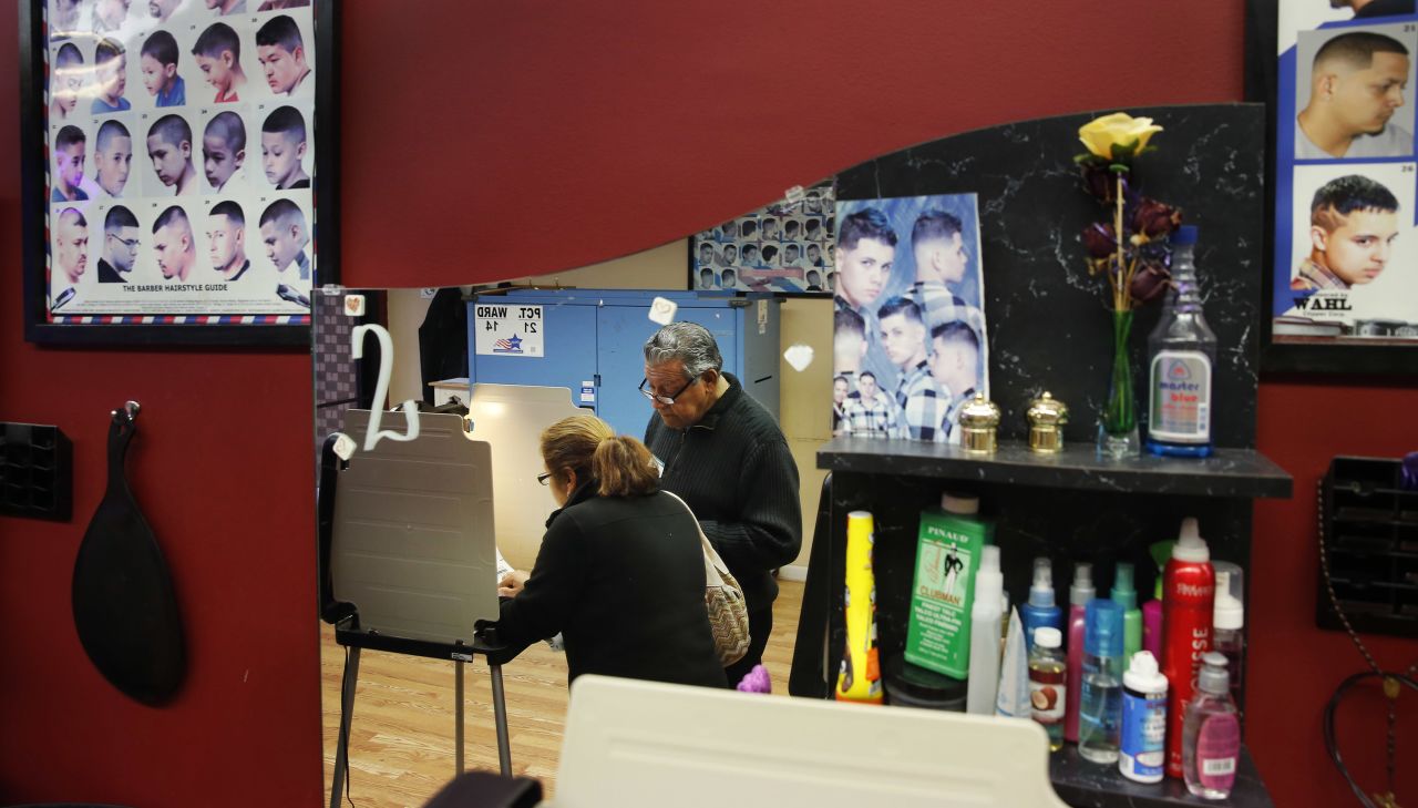 Democratic polling judge John Ramirez is reflected in a mirror as he helps a voter at a beauty salon in Chicago.
