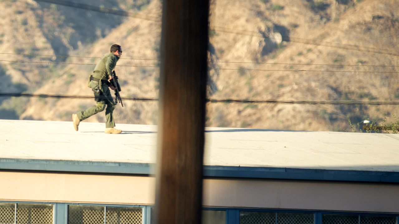 A SWAT team sniper moves atop a building to cover a suspect on Fourth Street in Azusa, California.