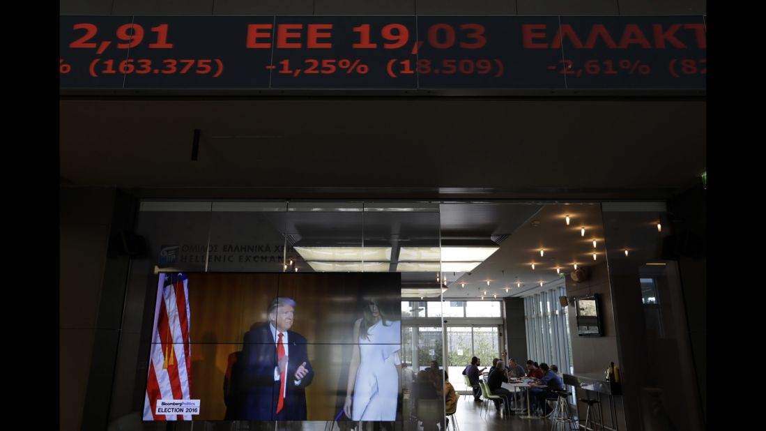 A stock ticker at the Athens Stock Exchange scrolls above a TV screen showing Trump on November 9.