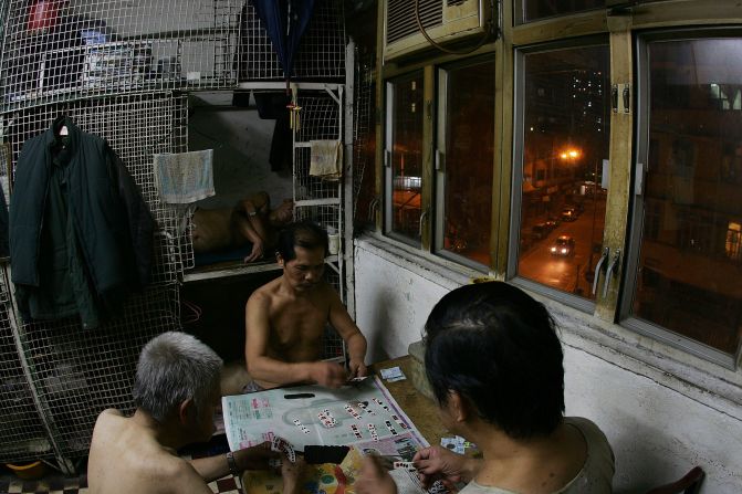 Apartments are usually divided by landlords into cages and rented out to tenants. Here, three men are pictured playing cards beside their cage homes.