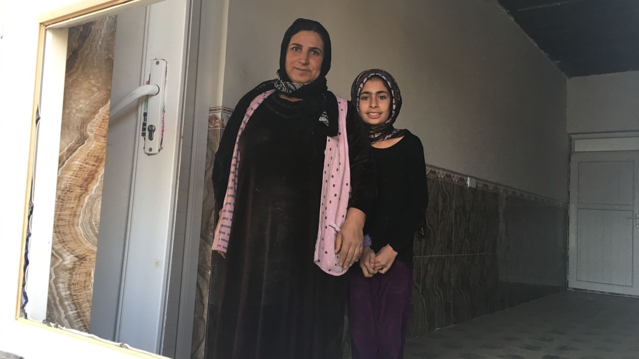 12-year-old Zena smiles next to her mother through the broken window of their home.