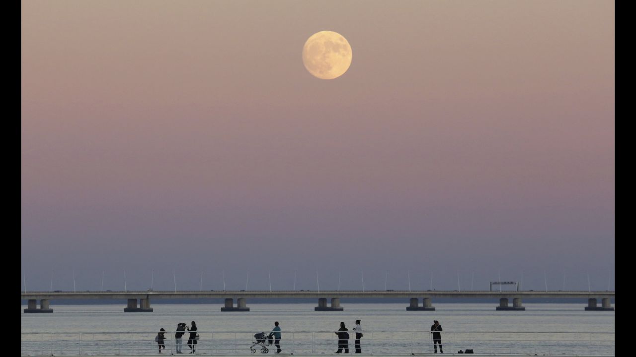 People stroll along the Tagus riverside as the moon rises in Lisbon, Portugal, on November 13.