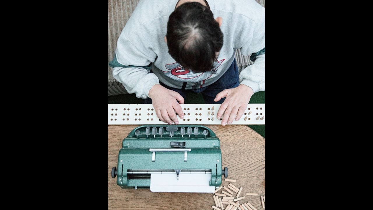 Jörg practices typing on a braille typewriter. His parents made him a wooden board with small wooden pins so he can feel the letters.