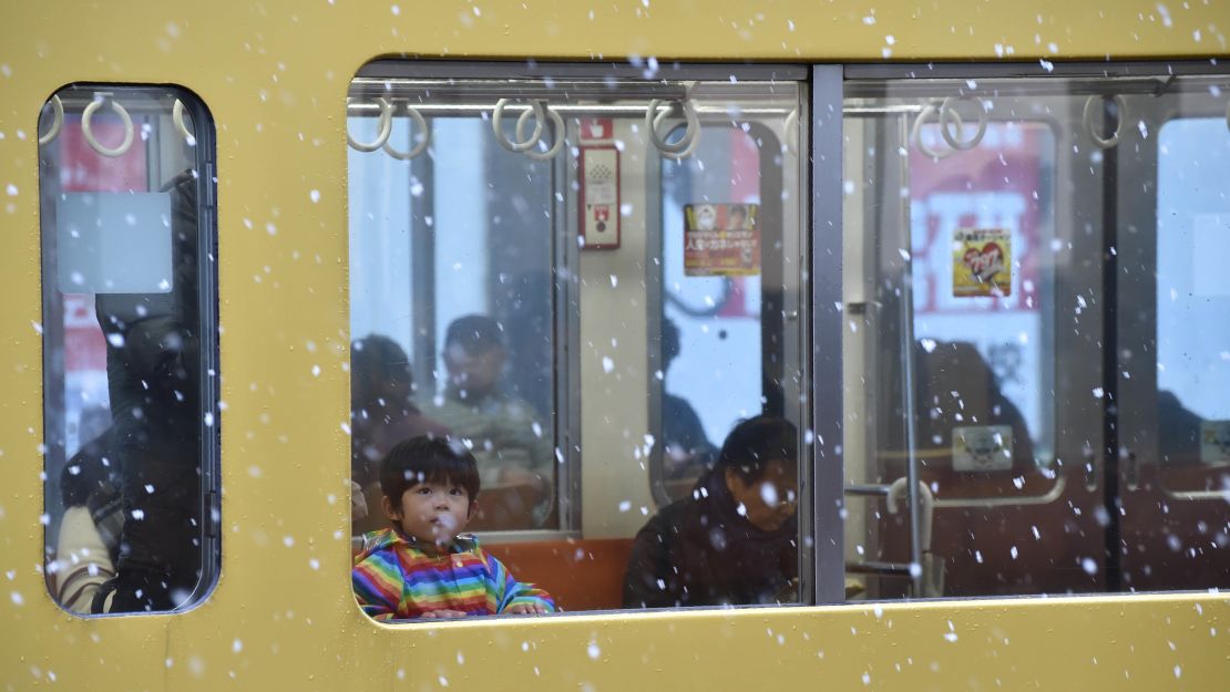 A boy looks at falling snow from a train window. 