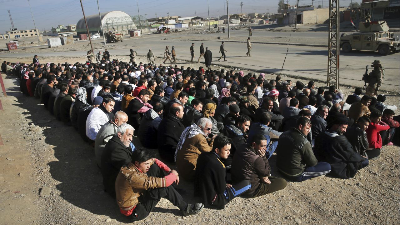 Iraqi civilians sit on the ground in Mosul on November 24. An Iraqi officer addressed the group, demanding to know the whereabouts of alleged ISIS militants who opened fire on troops a few days earlier.