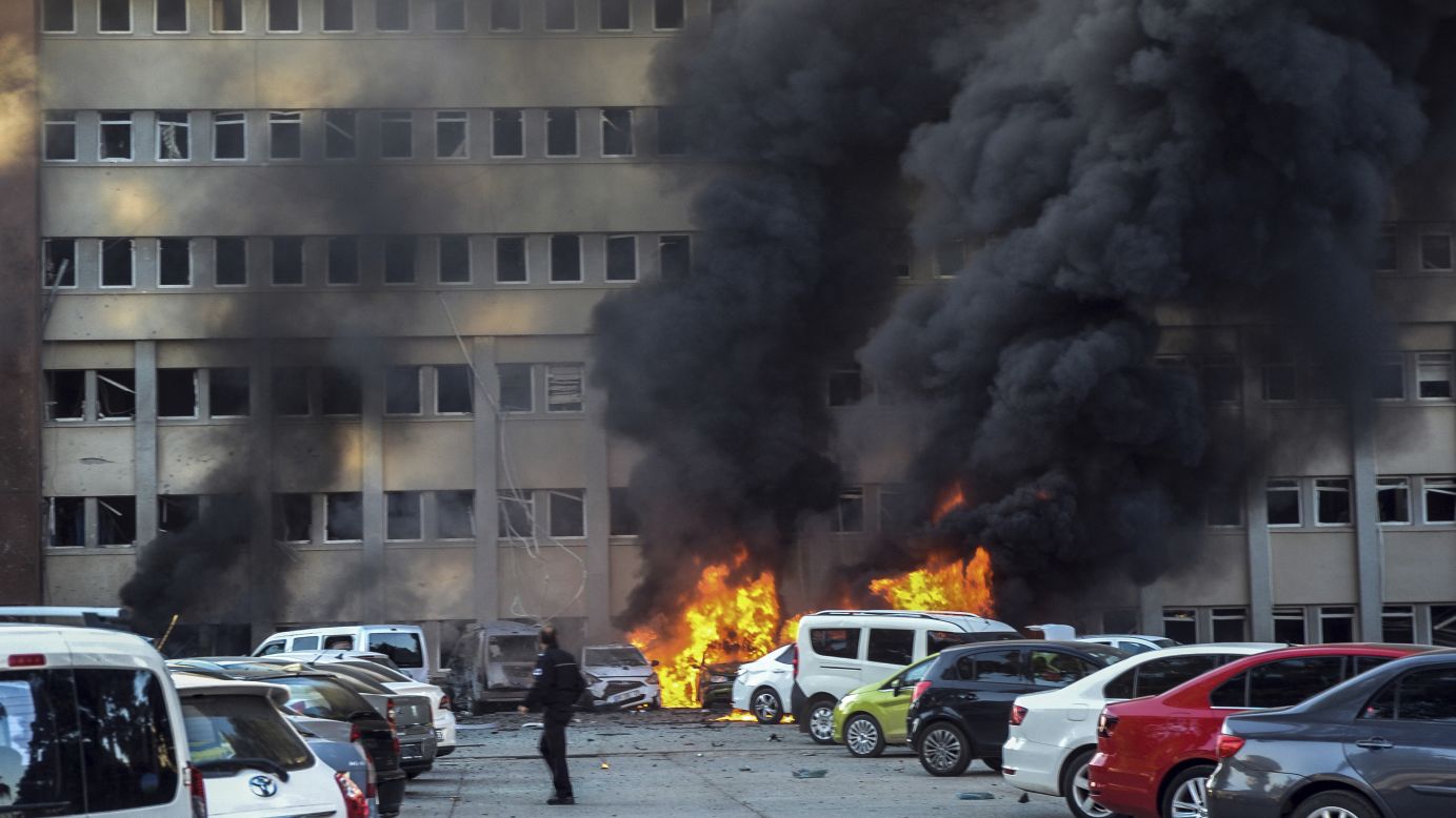 A police officer walks past a fire in Adana, Turkey, after a deadly explosion in the parking lot of a government building on Thursday, November 24.