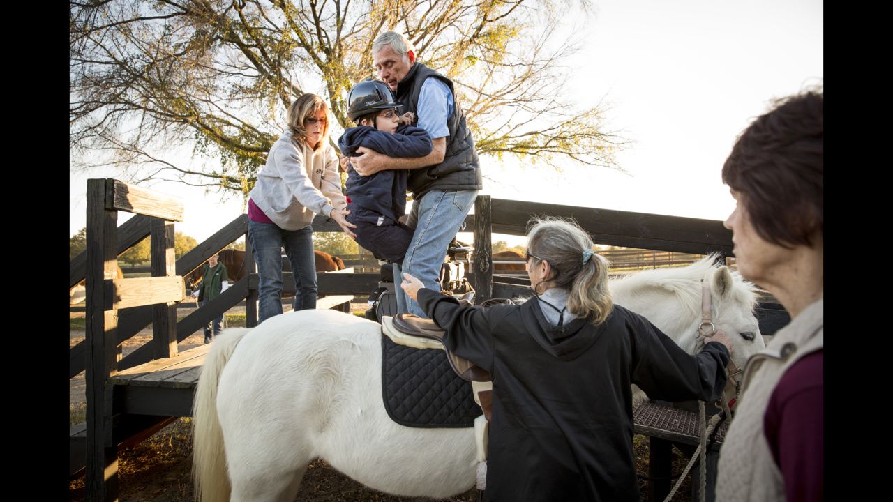Harry Swimmer helps place John, 13, on his horse for a group riding class, with help from his mother, Joy Simon and Jenny Tsering.