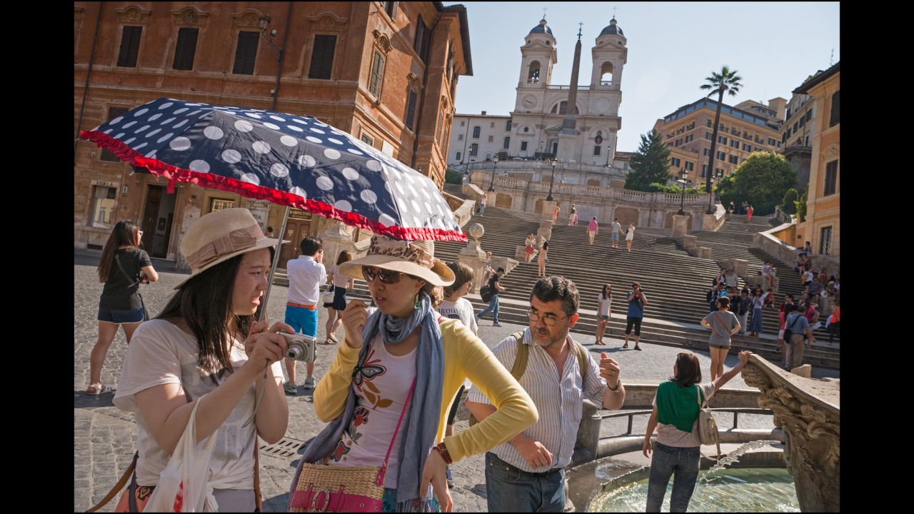 Tourists congregate in the Piazza di Spagna at the foot of the Spanish Steps with the Trinita dei Monti in the background.