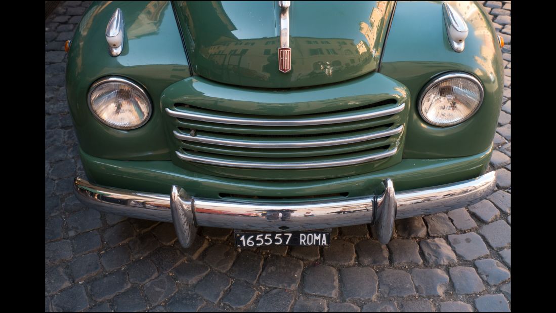 A classic Fiat car complete with old Roma plates looks at home on the cobbled street.  The number plates no longer contain the name of the city.