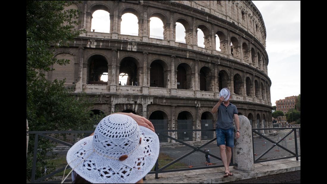A woman photographs a man in front of the Colosseum.