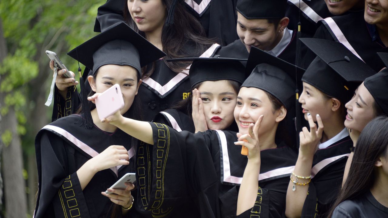 Chinese graduates dressed in academic gowns take a selfie during a photo shoot in Beijing, 23 May 2016.

