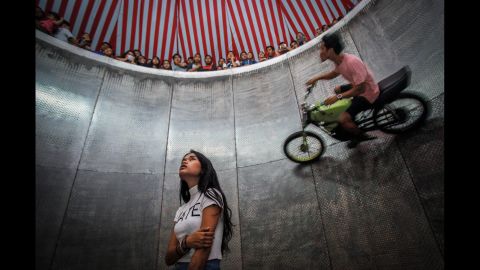 <strong>August 13:</strong> A young daredevil, center, waits for her turn as another person rides a motorbike around the "Devil's Barrel" at a carnival in Deli Serdang, Indonesia.