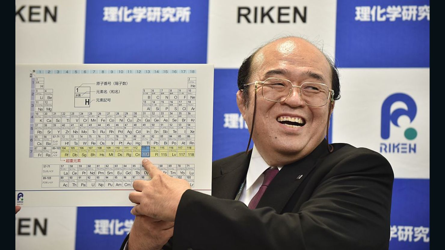 Kosuke Morita smiles as he points to a board displaying the new atomic element 113 during a press conference in Wako, Saitama prefecture, on December 31, 2015. 'Nihonium,' the name for the element, was officially approved Wednesday.