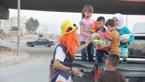 Anas al-Basha, dressed in his clown costume, plays with children on a roadside in Aleppo.
