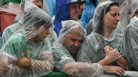 Somber fans in rain gear watch coffins enter Arena Conda stadium. 