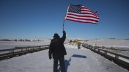 US Navy veteran John Gutekanst from Athens, Ohio, waves an American flag as an activist approaches the police barricade with his hands up on a bridge near Oceti Sakowin Camp on the edge of the Standing Rock Sioux Reservation on December 4, 2016 outside Cannon Ball, North Dakota.
Native Americans and activists from around the country gather at the camp trying to halt the construction of the Dakota Access Pipeline.  / AFP / JIM WATSON        (Photo credit should read JIM WATSON/AFP/Getty Images)