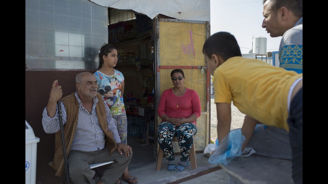 Raja Paulous, center, talks to neighbors at the entrance to her refugee camp grocery.