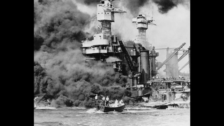 Pearl Harbor, Hawaii. A small boat rescues a seaman from the 31,800 ton USS West Virginia burning in the foreground. Smoke rolling out amidships shows where the most extensive damage occurred. Note the two men in the superstructure. The USS Tennessee is inboard