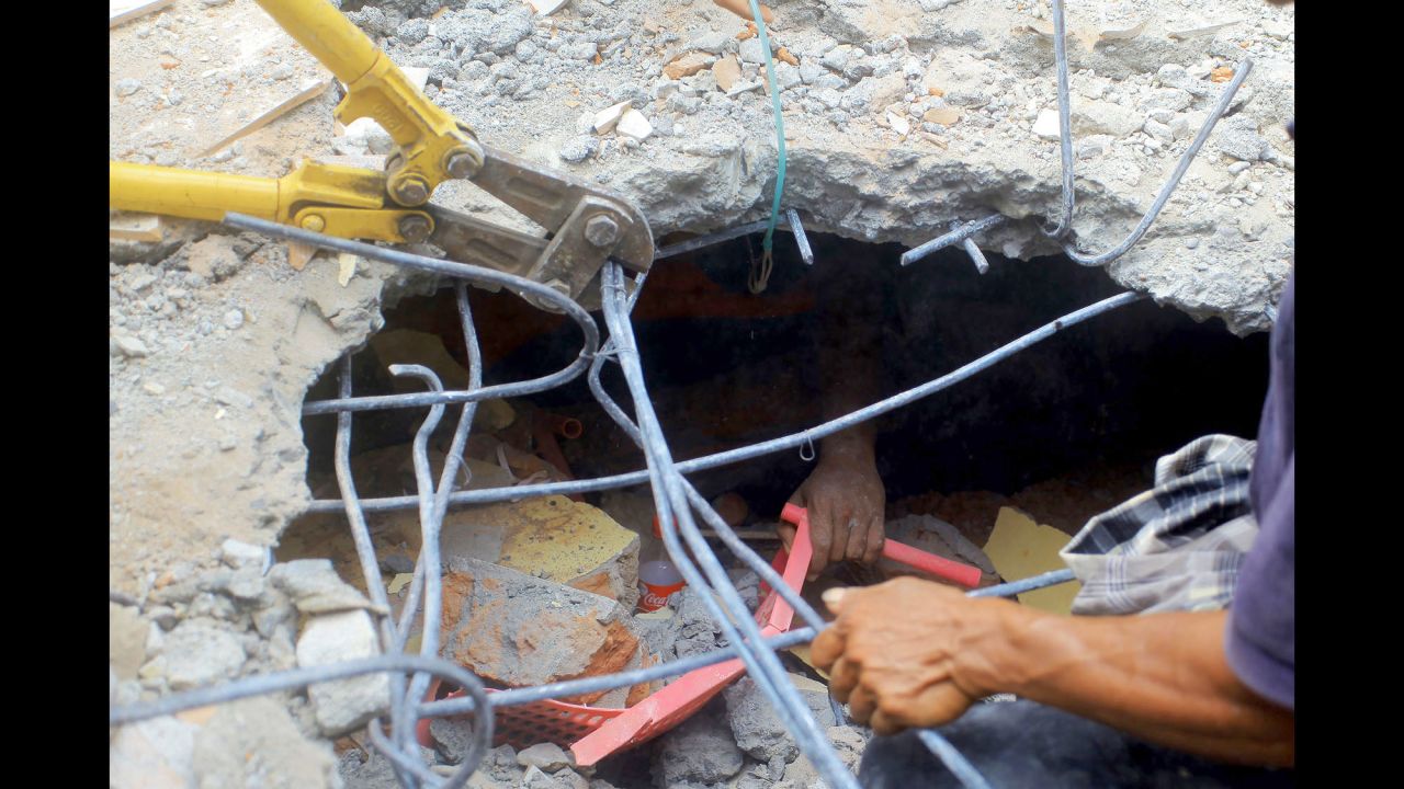 A survivor's hand reaches out from under a collapsed building while rescuers work to free the person.