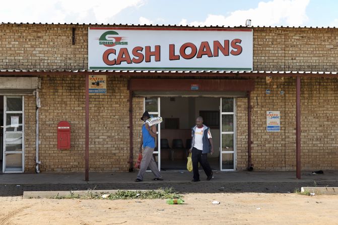 A broad majority of South Africans (62%) think the country's economic situation will improve in the next year. The study further found black South Africans to be significantly more optimistic than mixed-race and white South Africans.<br /><br />Pictured here, people walk in front of a Cash Loan shop in Marikana in April 2014. 