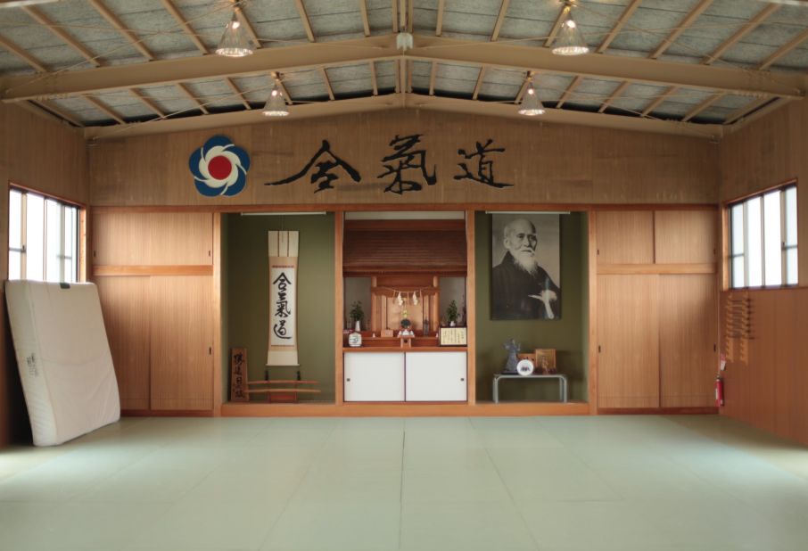 A photograph of aikido creator Morihei Ueshiba hangs on the wall at Aikido Tanabe Dojo. The blue, red and white logo is the official symbol of the International Aikido Foundation.  