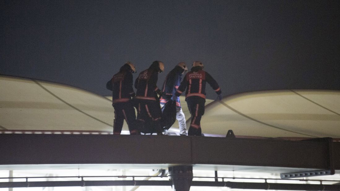 Firefighters carry a dead body through the roof of the stadium at the scene of the explosions.