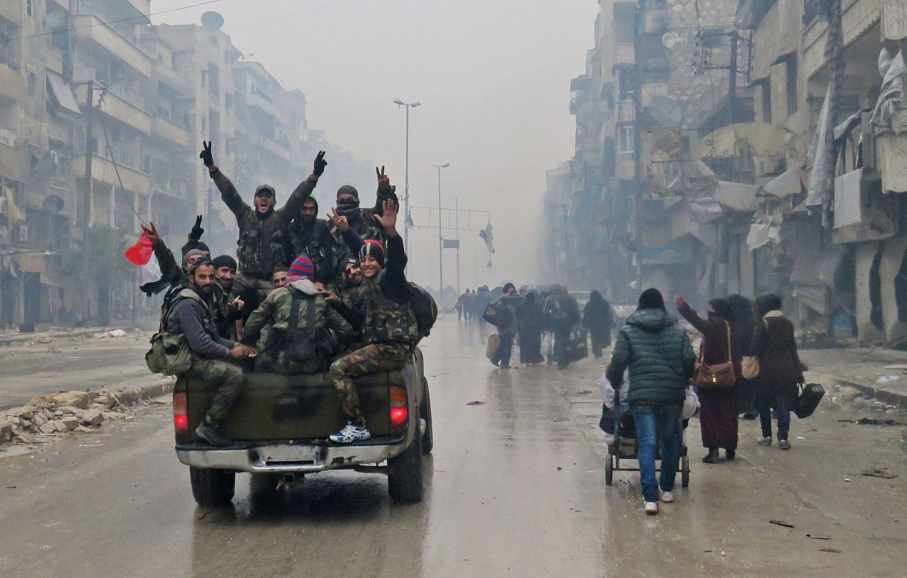 Pro-government fighters wave from a truck as they pass civilians fleeing the Bustan al-Qasr neighborhood on December 13.