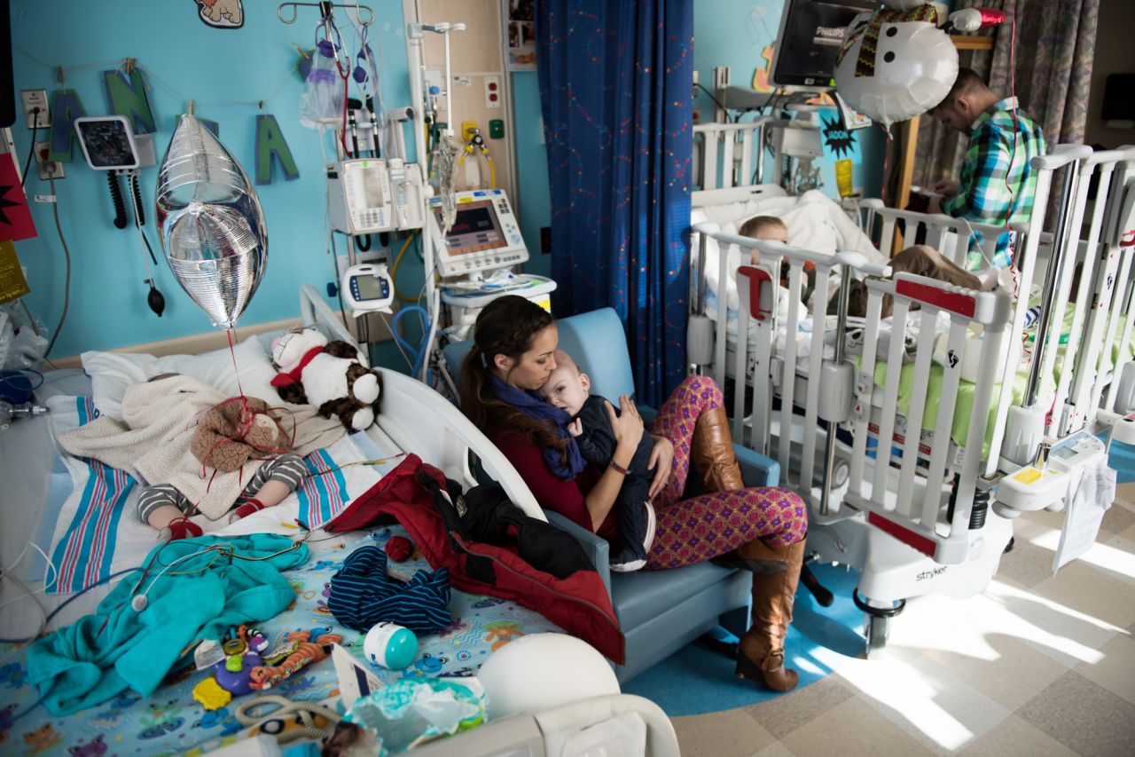 Nicole McDonald holds Anias as his twin brother, Jadon, sleeps in the bed to the left. The twins' older brother, Aza, watches television at the hospital from one of the boys' beds shortly before they left for rehab.
