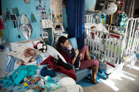 Nicole McDonald holds Anias as his twin brother, Jadon, sleeps in the bed to the left. The twins' older brother, Aza, watches television at the hospital from one of the boys' beds shortly before they left for rehab.