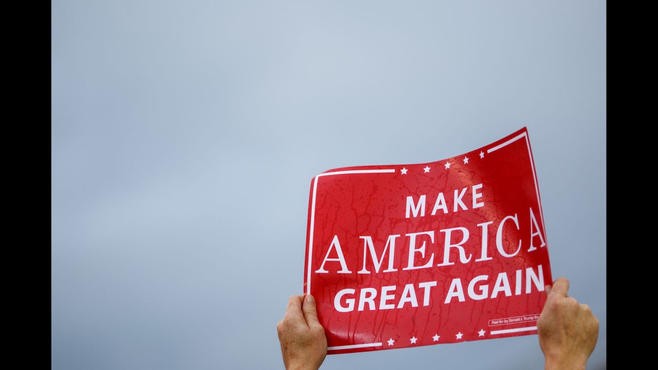 A Trump supporter holds up a rain-soaked "Make America Great Again" sign.
