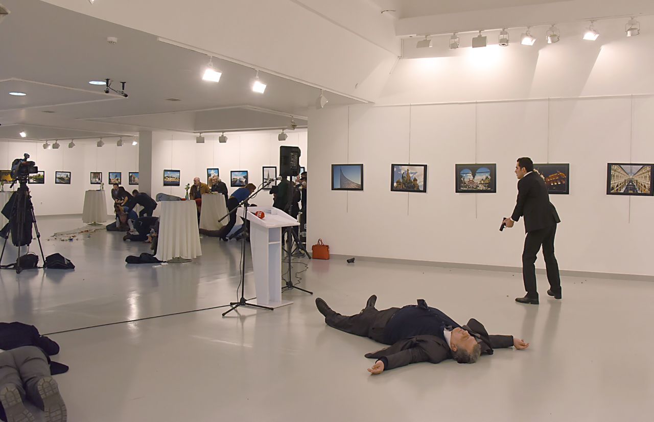 Karlov's body lies on the floor as the gunman stands nearby. 