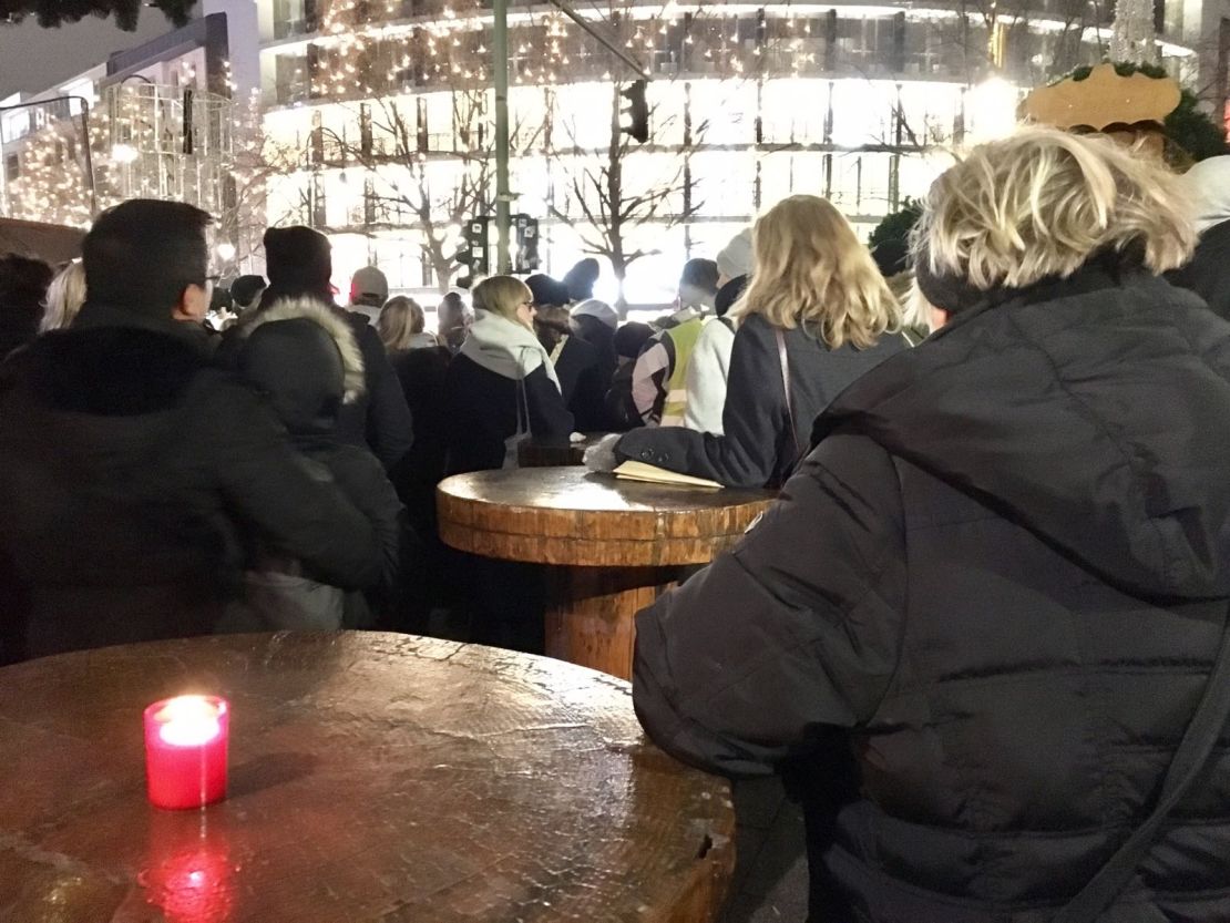 Mourners gather around tables at the closed Christmas market to listen to the service inside the Memorial Church.
