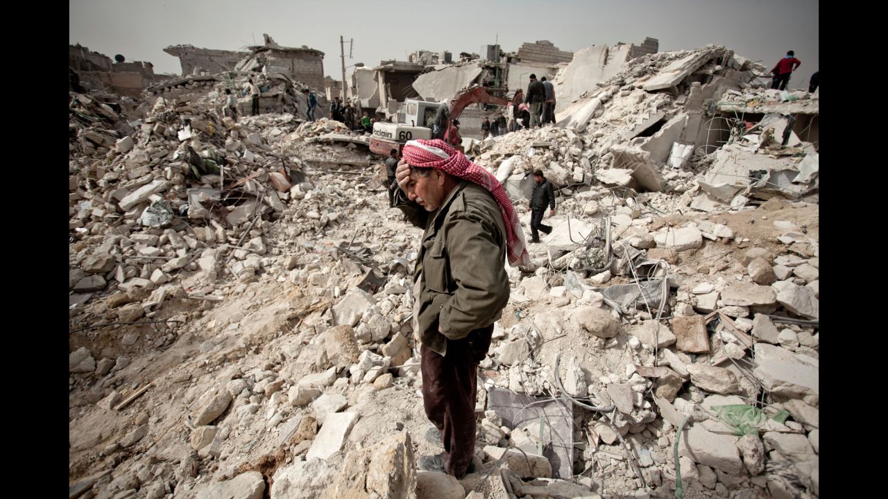 A Syrian man reacts while standing on the rubble of his house while others look for survivors and bodies in the Tariq al-Bab district of the northern city of Aleppo on February 23, 2013.
