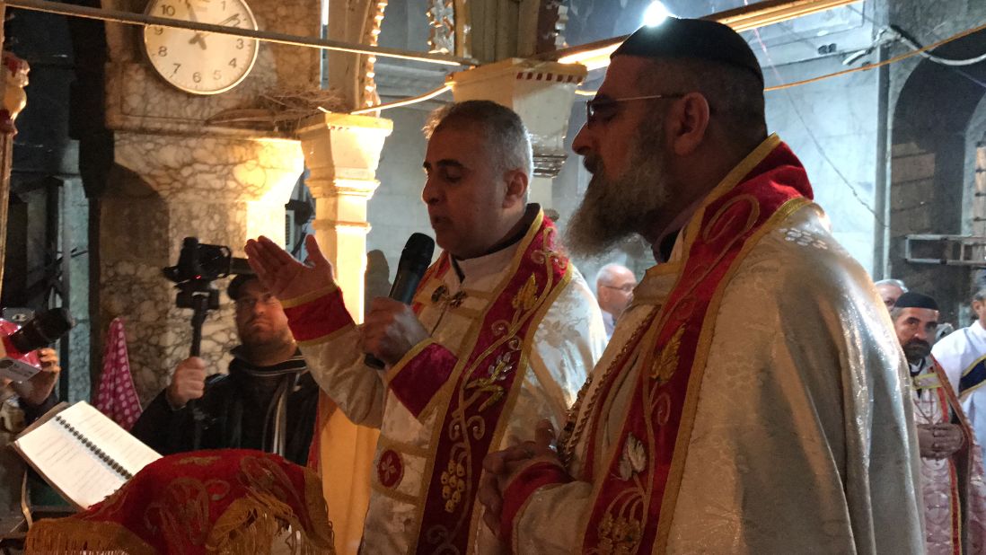 Father Behnam Lalo, left, and another clergyman pray during Christmas Mass held in Bartella.