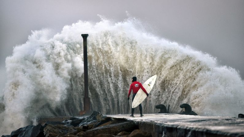 Professional surfer Al Mennie watches as a huge wave crashes against Castlerock pier during Storm Barbara in Coleraine, Northern Ireland, on Thursday.
