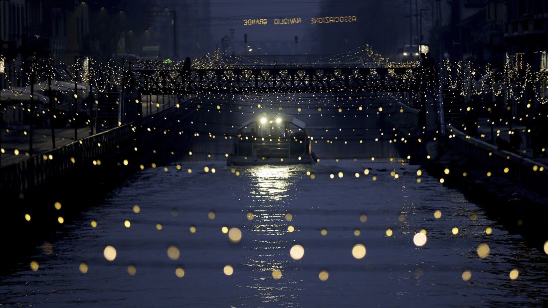 A tourist boat sails beneath Christmas lights illuminating Darsena dei Navigli, a Milan neighborhood named for the canals that run through it.